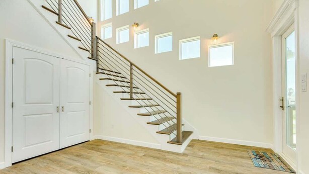 A spacious room with a wooden staircase, white walls, and a large window. - New 5BR Beach House with Dual Decks and Fire Pit (Surfside Beach)