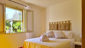 Ein Hotelzimmer mit Bett, Vorhängen am Fenster, einem Nachttisch und Blick auf Grünfläche.