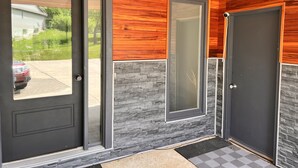 Une entrée moderne avec une porte sombre, une fenêtre en verre et un mur d’accent en pierre.