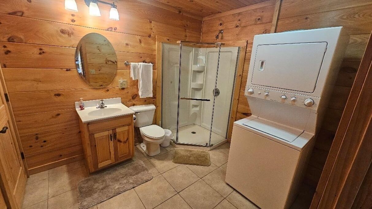 A wooden cabin bathroom with a sink, toilet, shower, and a white appliance.