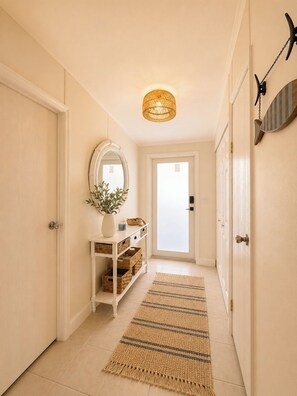 A hallway with a white door, a mirror, a wicker light fixture, and a striped rug. - Canal Waterfront ocean side w boat ramp & Hot Tub. Sleep 8 in Key Largo (Key Largo)