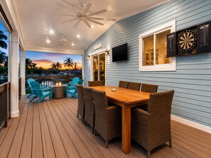 A covered patio with a wooden deck, wicker furniture, a flat-screen TV, dartboards, and a view of palm trees at sunset. - Canal Waterfront ocean side w boat ramp & Hot Tub. Sleep 8 in Key Largo (Key Largo)