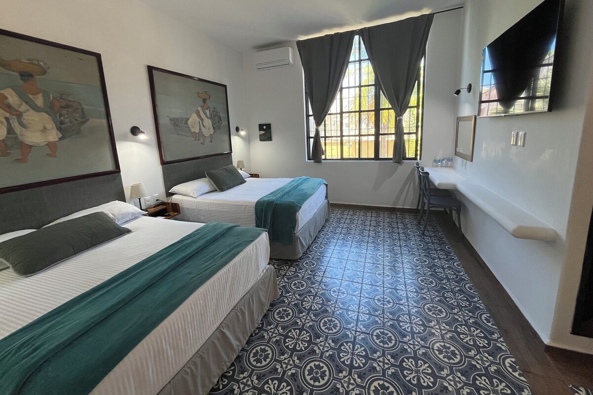 A hotel room with two beds, a desk, a chair, a TV, and a window with curtains.
