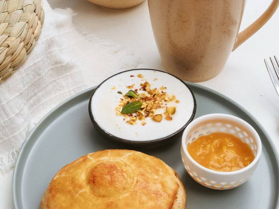 A plate with a pastry, a cup of coffee, a bowl of chips, and a small bowl of sauce.