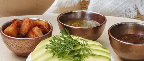 Una tabla de quesos con rebanadas de aguacate y hierbas, acompañada de tazones de totopos y salsas.