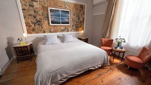 Un dormitorio con una cama grande, dos mesitas de noche, una silla, una pared decorada con un collage de fotos y una ventana con cortinas.