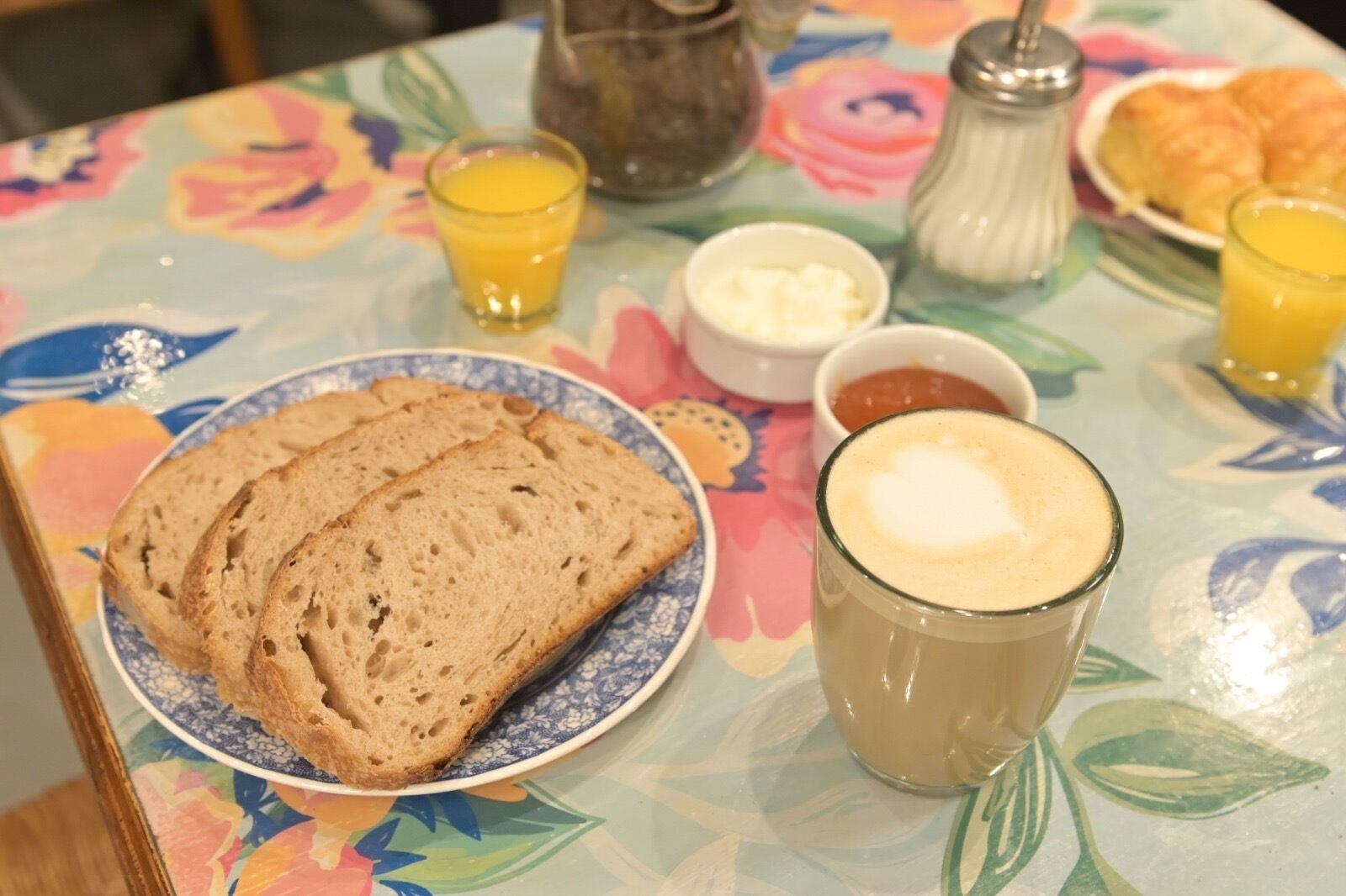 A breakfast table with bread, butter, jam, and a coffee drink.
