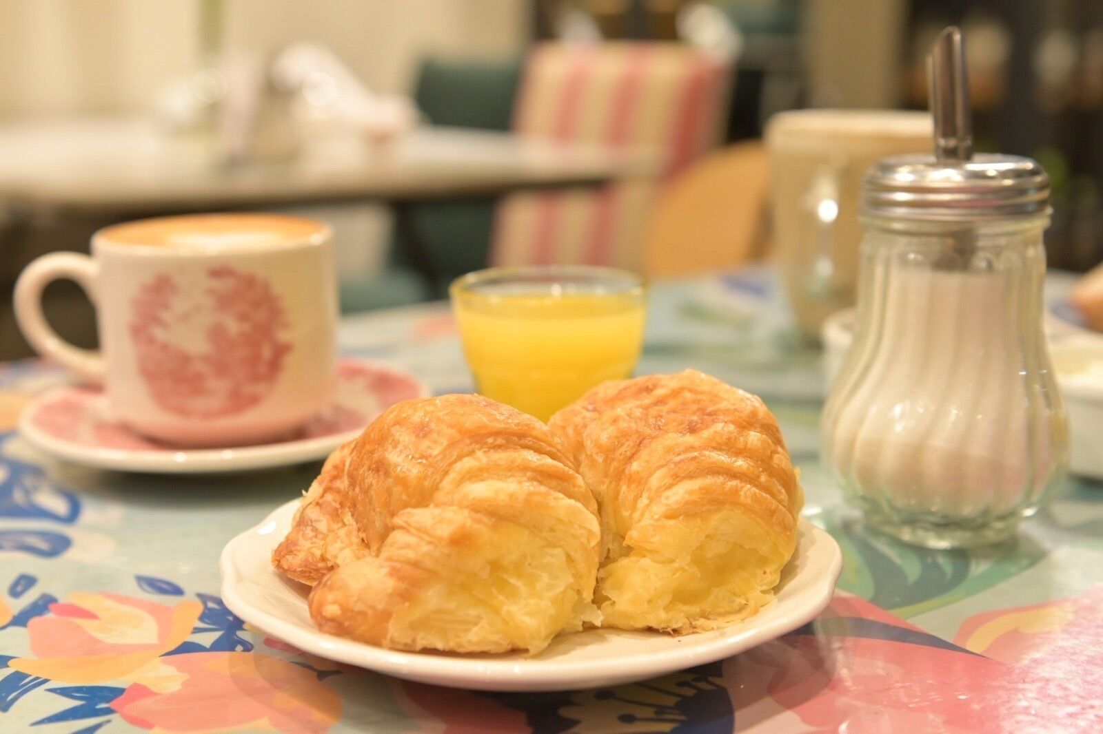 Ein Frühstückstisch mit Croissants auf einem Teller, einer Tasse Kaffee und einem Glas Orangensaft.