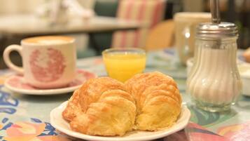 Une table dressée pour le petit-déjeuner, avec des croissants sur une assiette, une tasse de café et un verre de jus d’orange.