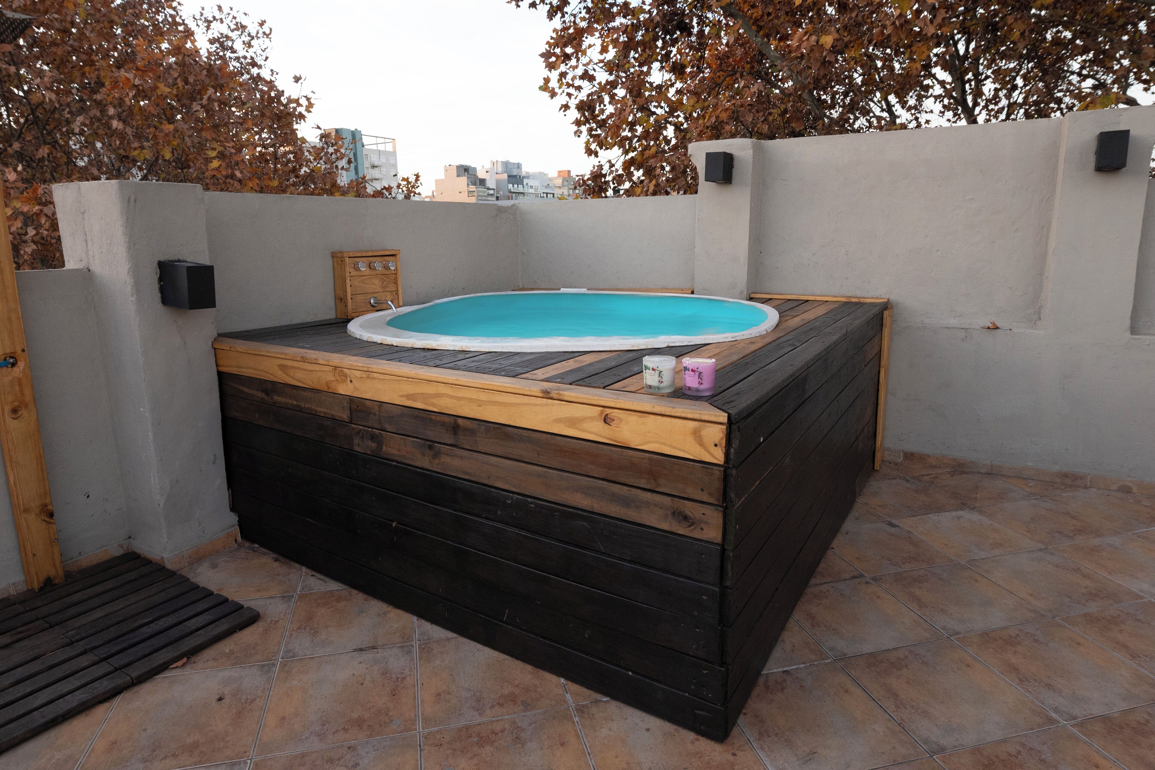 Un jacuzzi con revestimiento de madera, situado en un patio empedrado con vistas a la ciudad.