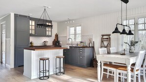 A modern kitchen with a central island, bar stools, a dining table with chairs, and a hanging light fixture. - 3 bedroom beautiful home in Sölvesborg (Sölvesborg)