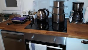 A compact kitchen with a stove, coffee maker, and stacked pots.