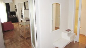 A room with a wooden floor, a white bench, a small table, and a mirror on the wall.