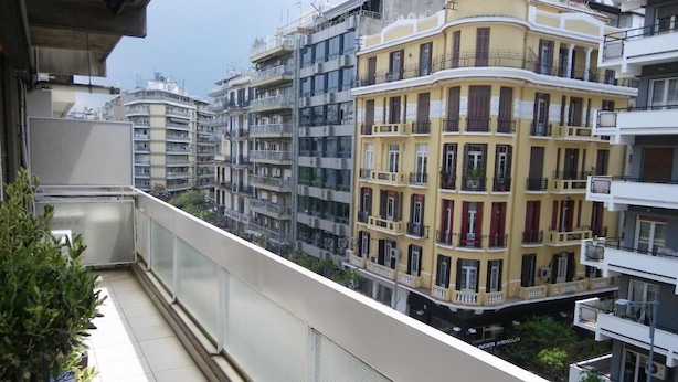 A balcony with a potted plant, overlooking a row of multi-story buildings with balconies.