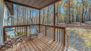 A wooden deck with two chairs and a table, overlooking a forest with autumn-colored trees. - Namba Cabin - Our Cabin (Great Cacapon)
