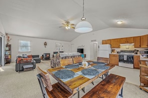 A spacious living area with a large wooden dining table, a sofa, a TV, and a kitchen with wooden cabinets and appliances. - Namba Cabin - Our Cabin (Great Cacapon)