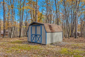 A small, single-story shed with a sloped roof and blue doors, surrounded by a forest with autumn-colored trees. - Namba Cabin - Our Cabin (Great Cacapon)