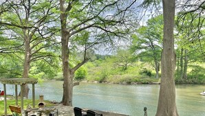 Um coreto com área de estar ao ar livre à beira de um rio, rodeado por árvores e vegetação.