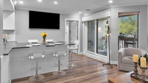 A modern kitchen with a bar area, white bar stools, and a dining table set for four. - 7104 Harbourside 1 @ Shelter Cove | Pool | Stunning Marina Views (Hilton Head Island)