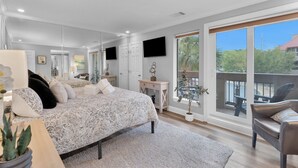 A modern bedroom with a large bed, a desk, a chair, and a balcony with a view. - 7104 Harbourside 1 @ Shelter Cove | Pool | Stunning Marina Views (Hilton Head Island)