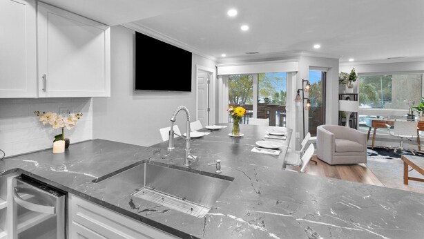 A modern kitchen with a marble countertop, stainless steel sink, and a dining area with a white chair and table. - 7104 Harbourside 1 @ Shelter Cove | Pool | Stunning Marina Views (Hilton Head Island)