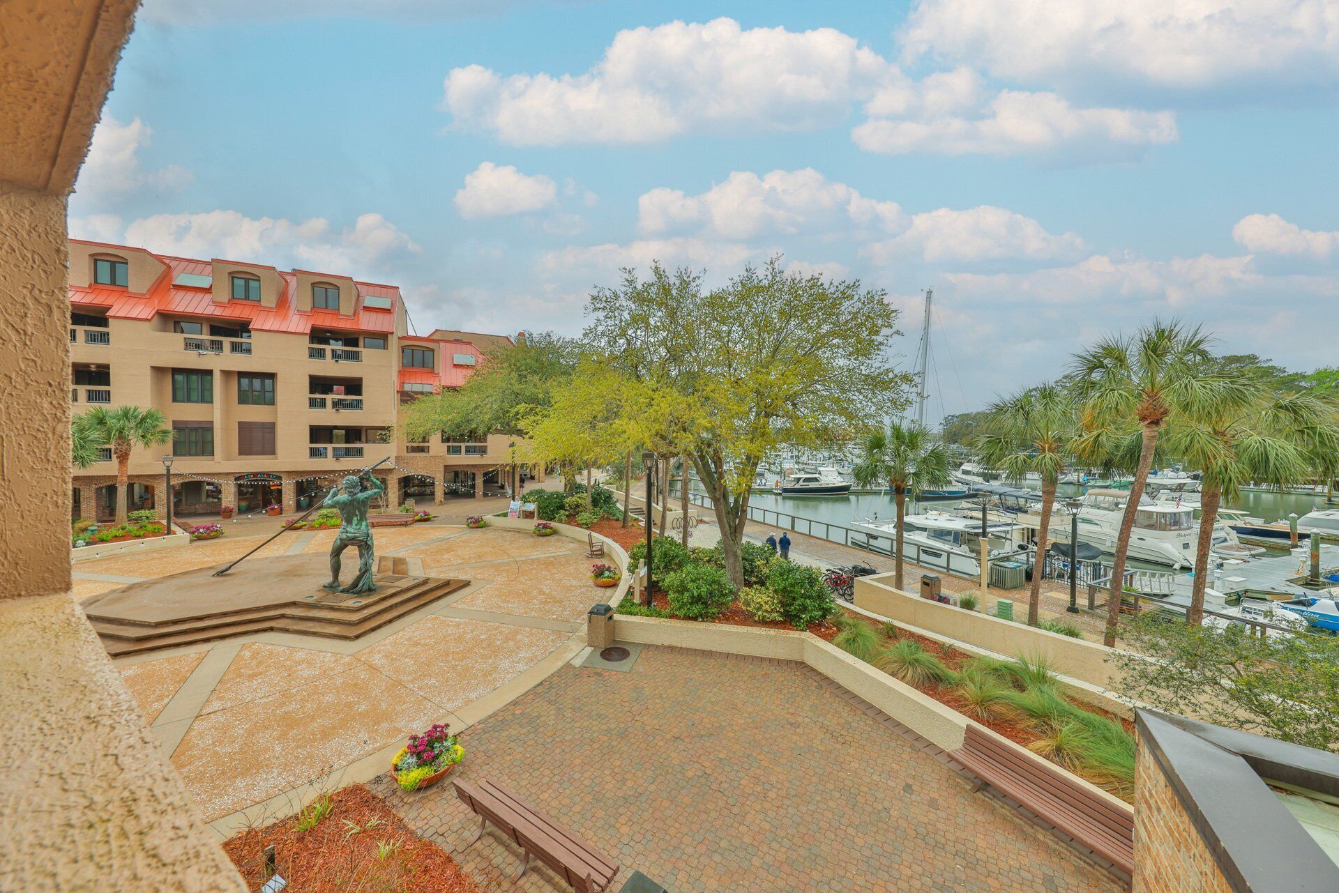 A courtyard with a statue, a view of boats, and a building with balconies.