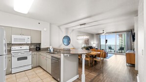 A modern kitchen with a central island, built-in appliances, and a dining area with a view of the balcony. - Ultimate Beachfront Condo Sleeps 10! Free Activities! Summer Deals! (Panama City Beach)