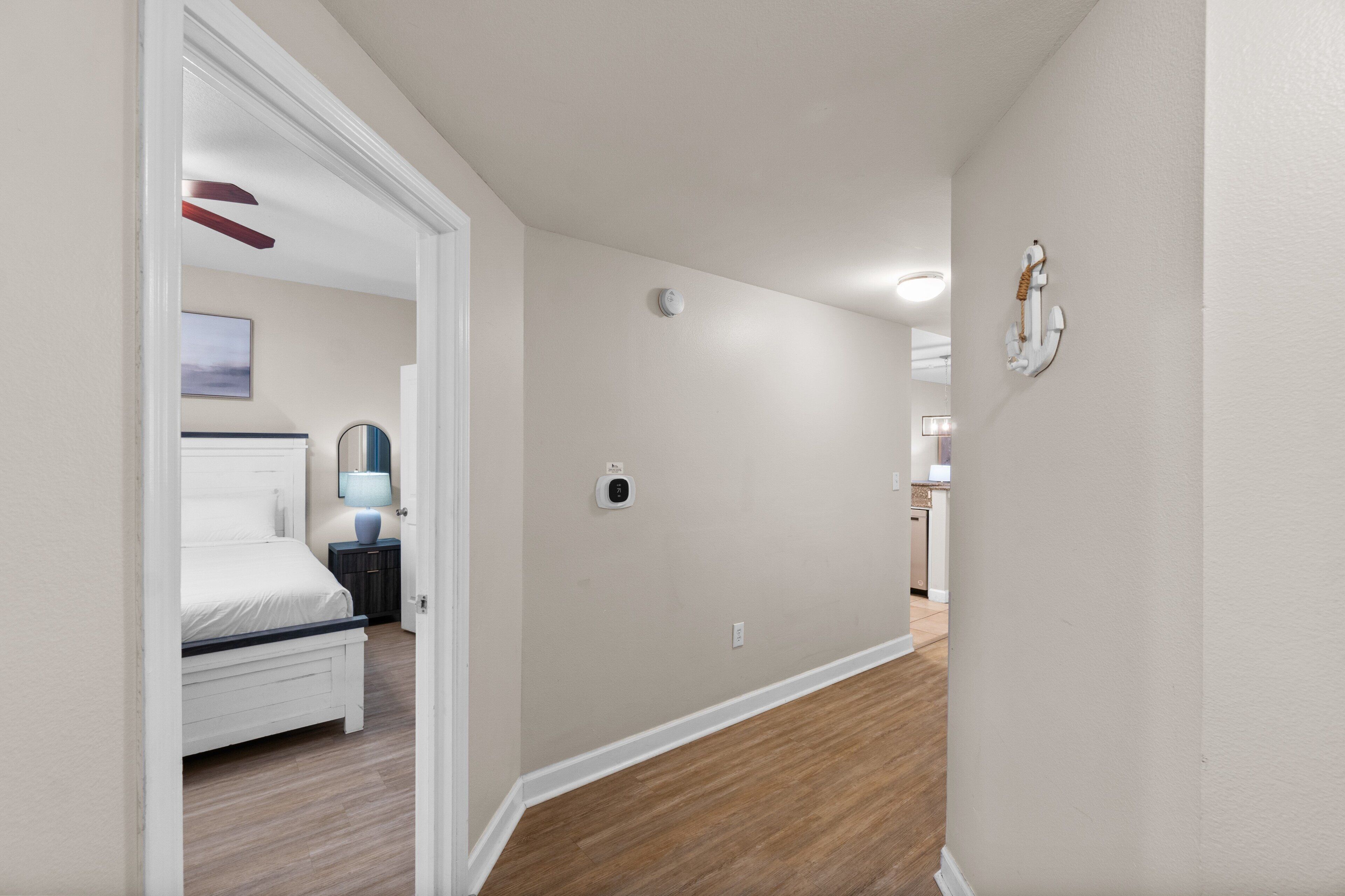 A hallway with a wooden floor, a white door leading to a bedroom, and a wall-mounted light fixture.