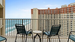 A balcony with two chairs and a small table, overlooking a beach and a high-rise building. - Ultimate Beachfront Condo Sleeps 10! Free Activities! Summer Deals! (Panama City Beach)