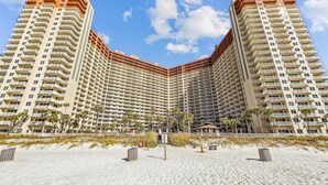 A high-rise hotel with a curved facade, multiple balconies, and a beachfront location. - Ultimate Beachfront Condo Sleeps 10! Free Activities! Summer Deals! (Panama City Beach)