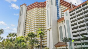 A multi-story hotel with a central tower and a parking garage. - Ultimate Beachfront Condo Sleeps 10! Free Activities! Summer Deals! (Panama City Beach)