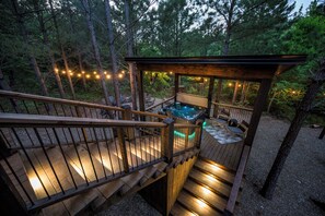 Een houten terras met een hottub, omringd door bomen en slingerrimpels.