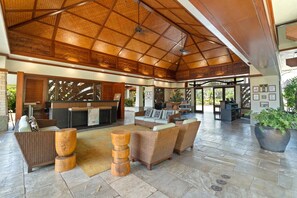 Eine geräumige Lobby mit hoher Decke, einem Empfangsbereich, bequemen Sitzgelegenheiten und einer großen Pflanze in einem Topf.