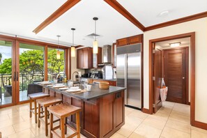 A modern kitchen with a central island, wooden bar stools, and a view of the outdoors.