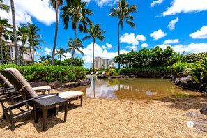 Ein Poolbereich eines Resorts mit Liegestühlen, Palmen und einem Gebäude im Hintergrund.