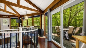 A wooden deck with outdoor seating, a staircase, and large windows offering a view of greenery.