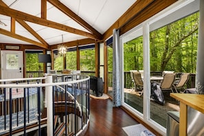 Une terrasse en bois avec des sièges d’extérieur, un escalier et de grandes fenêtres donnant sur un paysage verdoyant.