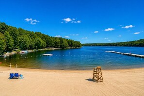 A sandy beach with a lifeguard chair, a clear blue sky, and a calm lake surrounded by trees. - Sleep in a Treehouse!! (Lake Ariel)
