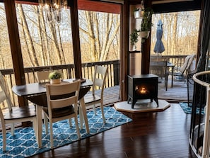 A wooden deck with a table and chairs, a wood-burning stove, and a view of leafless trees. - Sleep in a Treehouse!! (Lake Ariel)