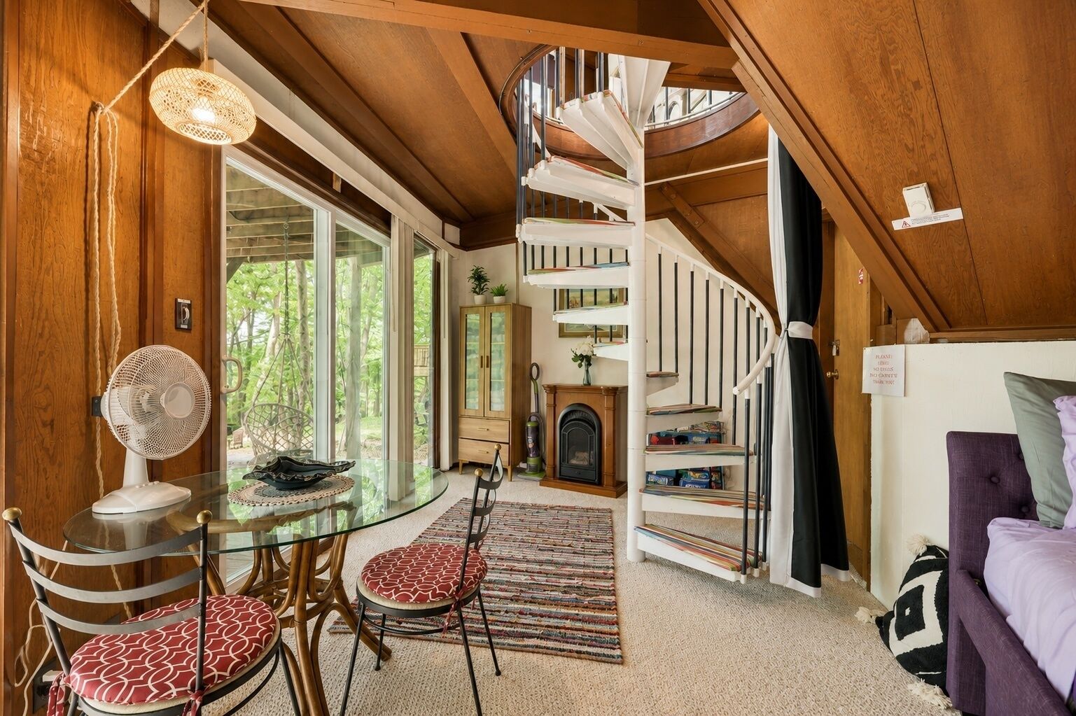 Un intérieur moderne avec un escalier en colimaçon, un coin repas doté d’une table en verre et une cheminée chaleureuse.