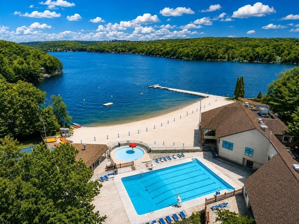 A resort with a swimming pool, beach area, and a view of a lake.