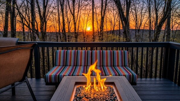 A deck with a fire pit, a striped bench, and a chair.