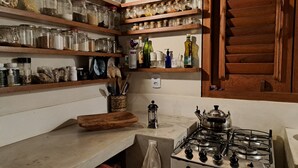 A kitchen with wooden shelves holding jars, bottles, and utensils; a gas stove; and a wooden cutting board. - Sol e Mar House - Front beach in Serra Grande (Itacaré)