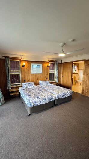 A bedroom with a large bed, wooden walls, a ceiling fan, and a window with curtains.