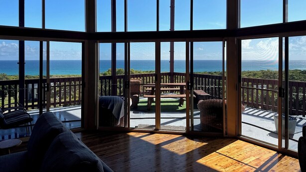 A spacious room with large windows offering a view of the ocean. - Ocean View Holiday Home Orchid Beach | Phippsy's On Fraser | Sleeps 20 people! (K'gari)