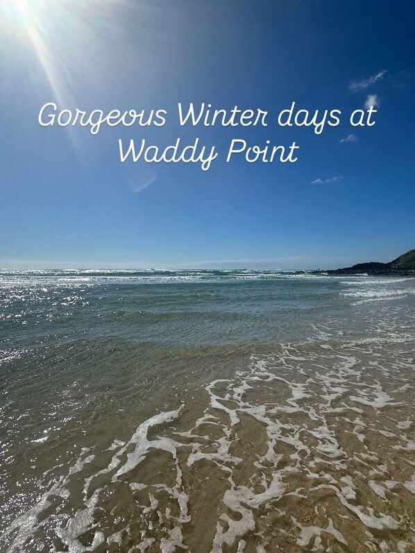 A beach scene with clear skies and calm waters, labeled "Gorgeous Winter days at Waddy Point".