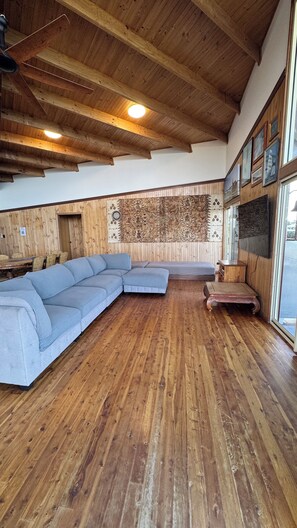 Una habitación amplia con techo de madera, un sofá modular grande, una mesa de centro de madera y un panel decorativo en la pared.