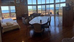 A spacious room with a large dining table and chairs, a bed with a striped comforter, and a view of the ocean through large windows. - Ocean View Holiday Home Orchid Beach | Phippsy's On Fraser | Sleeps 20 people! (K'gari)