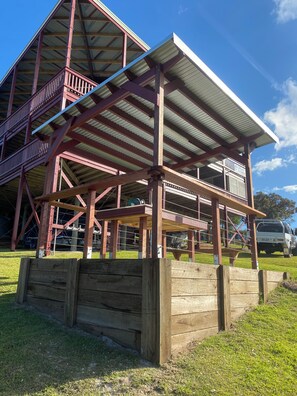A large wooden structure with a metal roof, possibly a barn or a pavilion, with a grassy area in front.