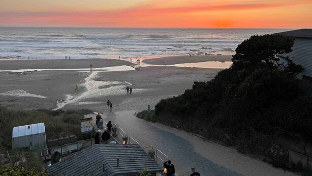 A beach with a path leading to the water, a sign indicating a viewpoint, and a small building in the foreground.
